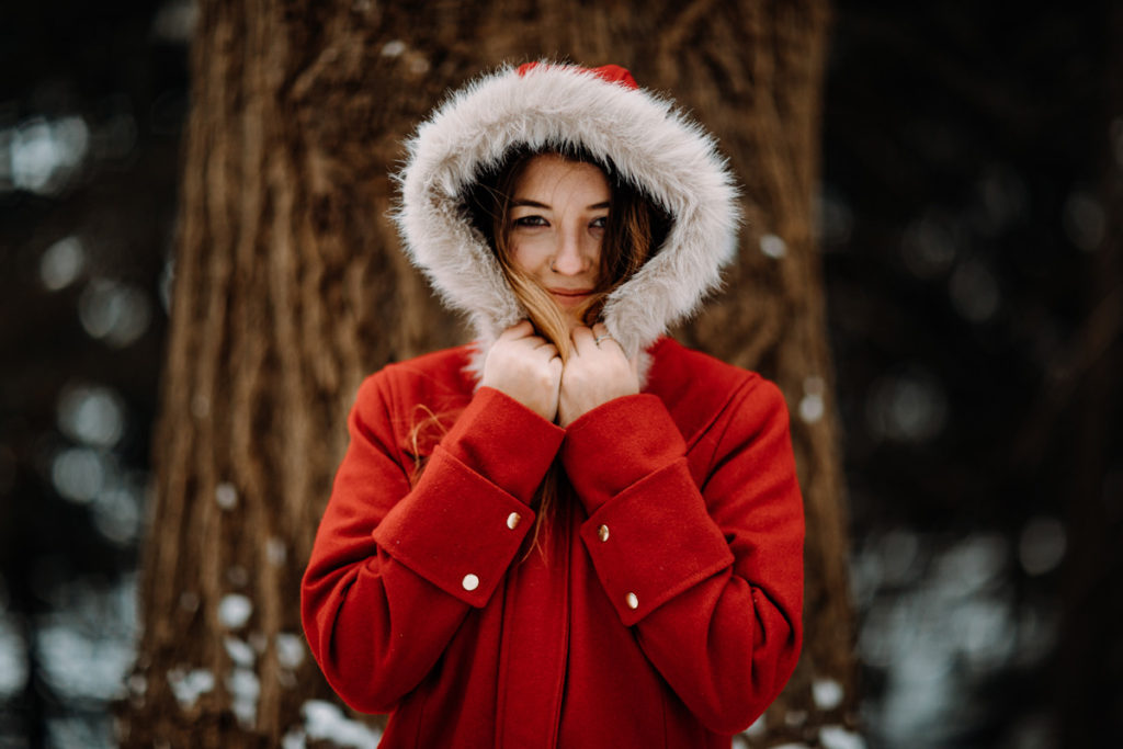 portrait of a girl in a hooded red coat in front of a tree with snow on the ground