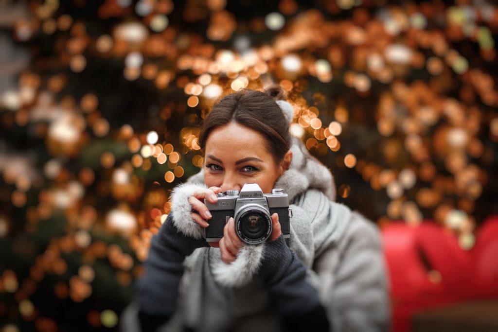 girl taking a picture with christmas lights behind her