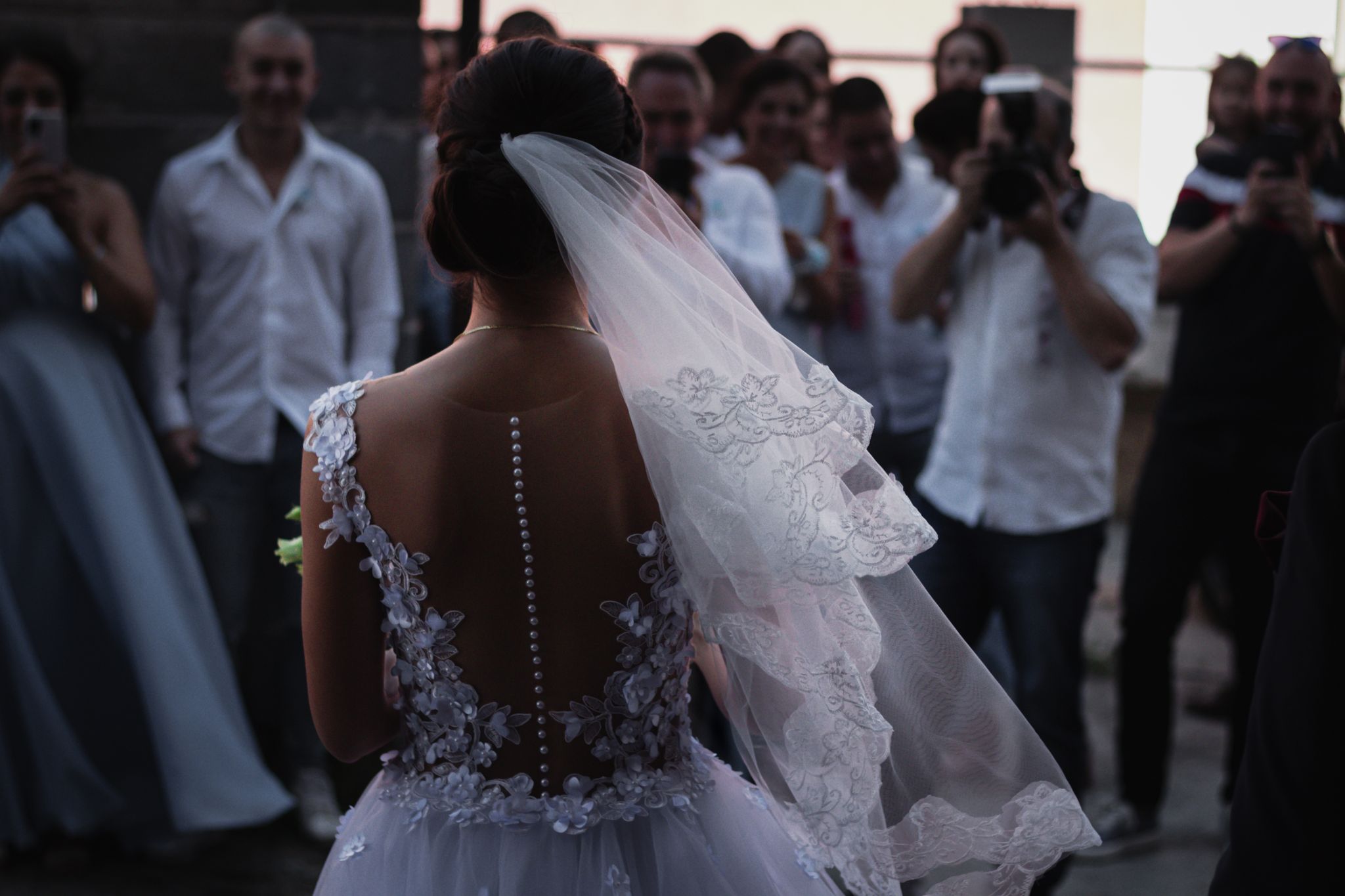 A bride in a white lace dress stands before a crowd at her wedding ceremony, creating a romantic moment.