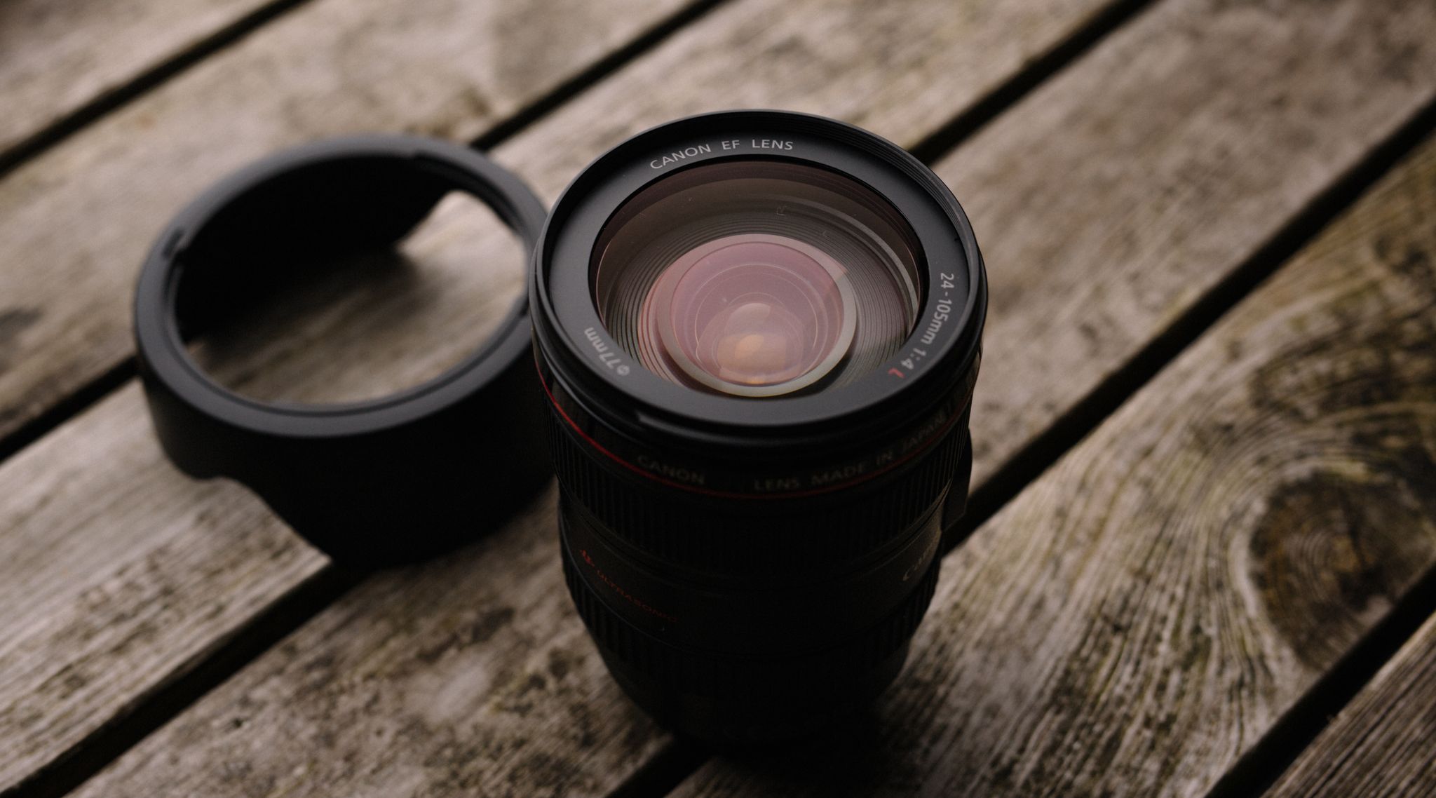 Close-up of a Canon EF lens with hood on a rustic wooden table, ideal for photography themes.