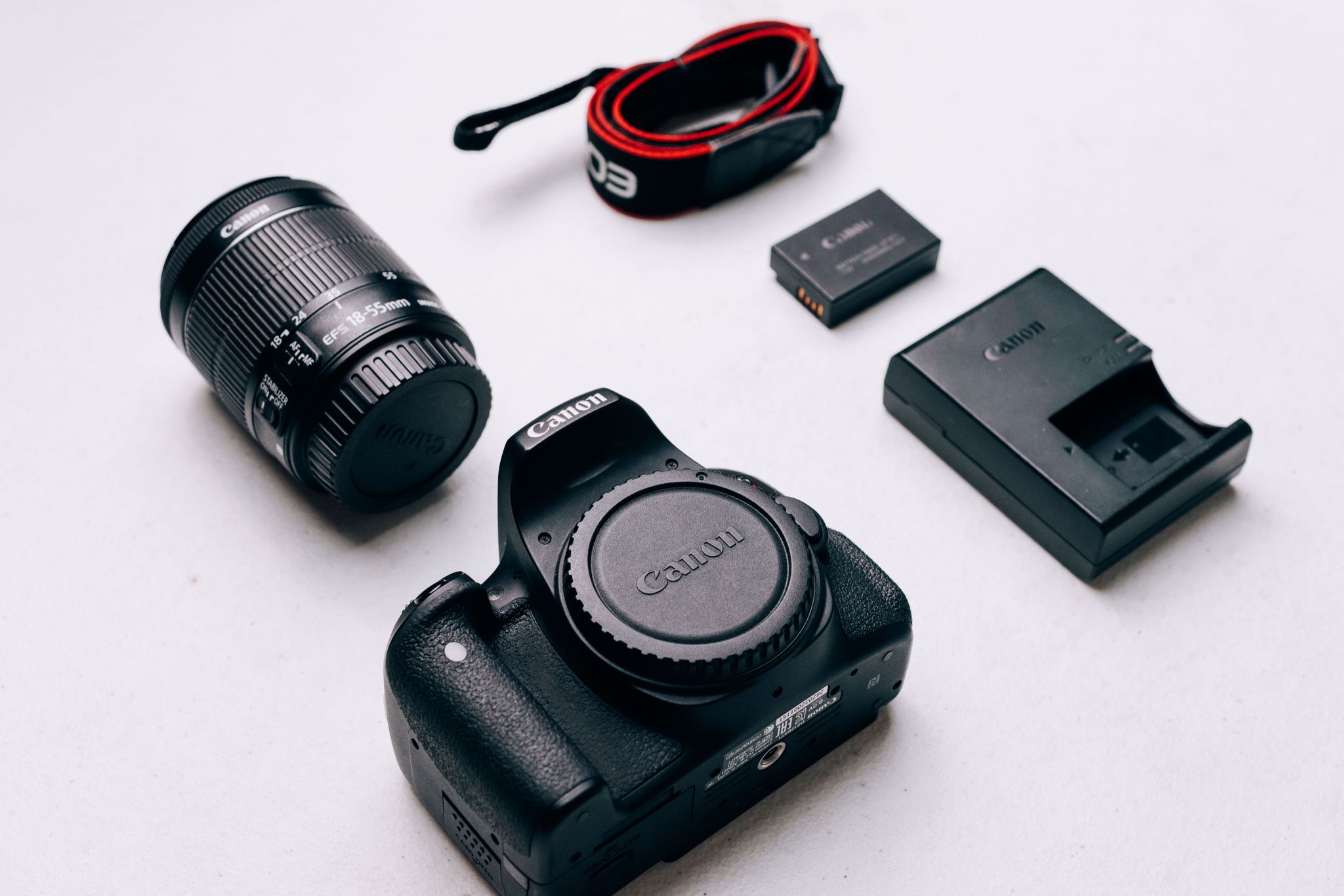 Flat lay of Canon DSLR camera accessories including lens, battery, and charger on a white background.